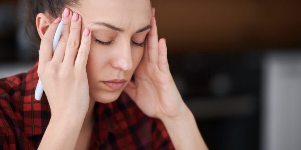 Young tired brunette woman with pen touching her temples and keeping her eyes closed while trying to concentrate