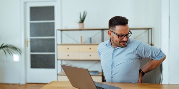 Man having pain in back. He holding it by hand while sitting at table during job.